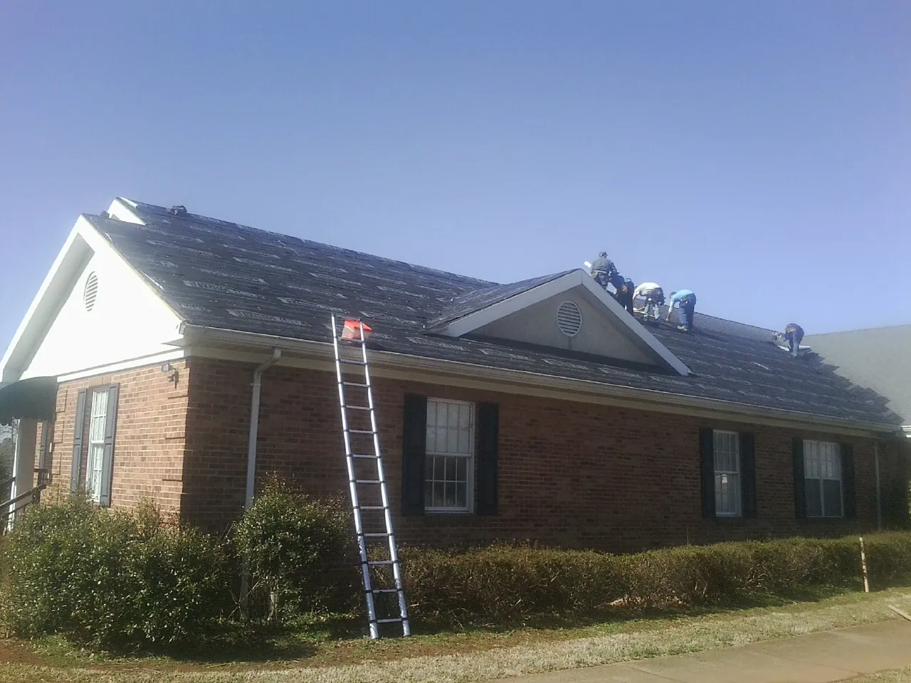 Crew tearing shingles off a brick ranch roof with a ladder set — Emergency Roof Repair work by our crew in Elloree