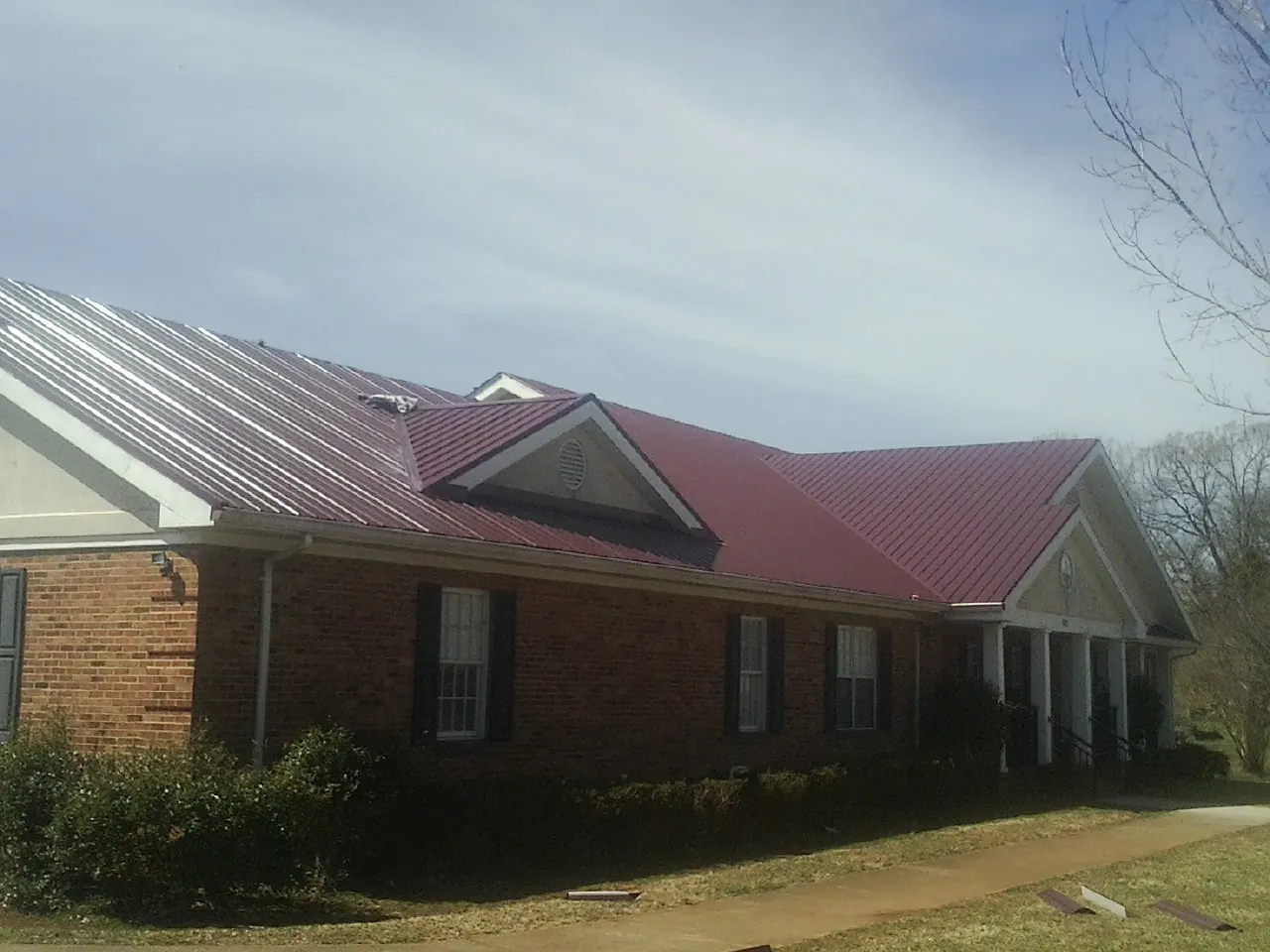 Red metal roof with gabled entries on a long brick building, from a Hail Damage Roof Repair job in Elloree