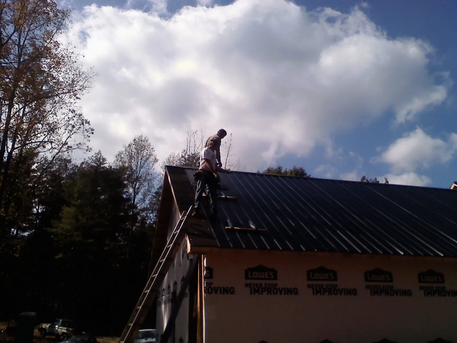 Roofer fastening dark metal panels high against a cloudy sky, from a Roof Inspection job in Elloree