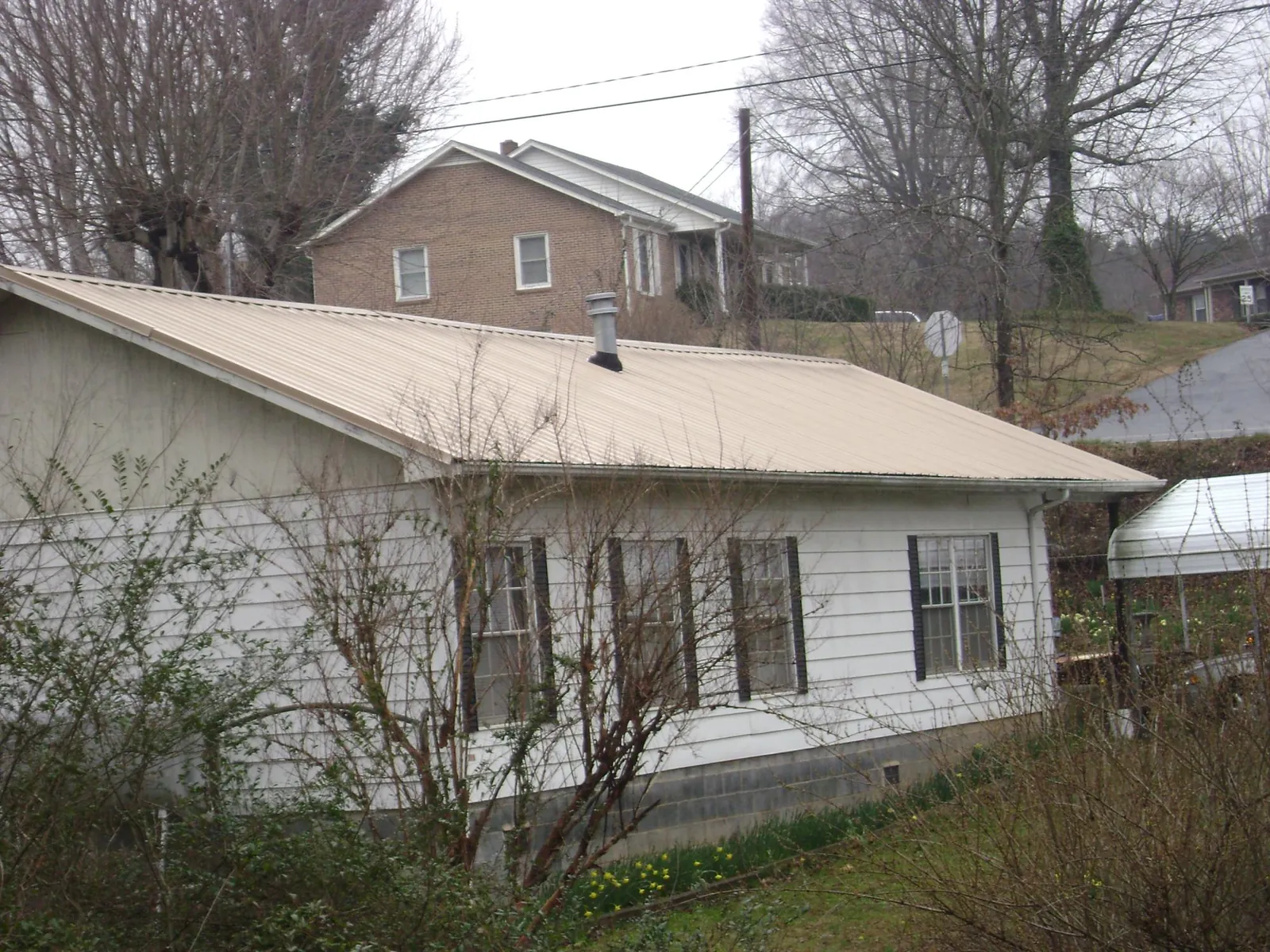 Tan metal roof on a white sided house set into a hillside — Commercial Roofing by Roofing Brothers in Elloree